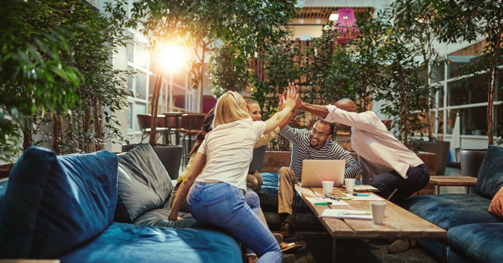 An image of a small group of people sitting at a table and high-fiving each other.