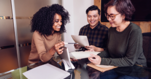 An image of 3 people smiling and working together at a desk.