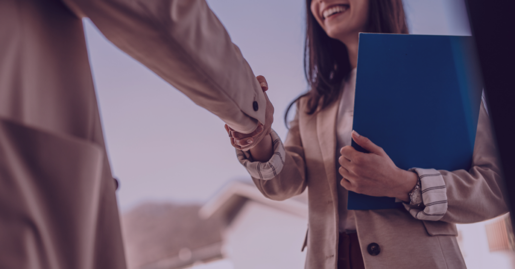 An image of a woman with a folder shaking someone's hand.